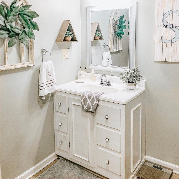 A small, farmhouse bathroom with a white vanity, mirror, towel, and decorative plants on shelves