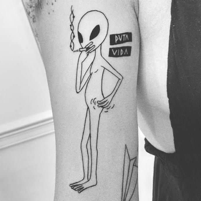 A black ink tattoo of a tall, skinny alien smoking a cigarette with 'Puta Vida' written beside it in bold letters.