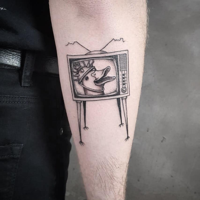 A black ink tattoo of an old TV with thin legs and antennas, displaying a duck with a spiky crown, blending surreal and humorous elements.