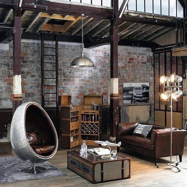 Industrial loft with brick walls, leather seating, a modern egg chair, metal decor, and a vintage airplane coffee table