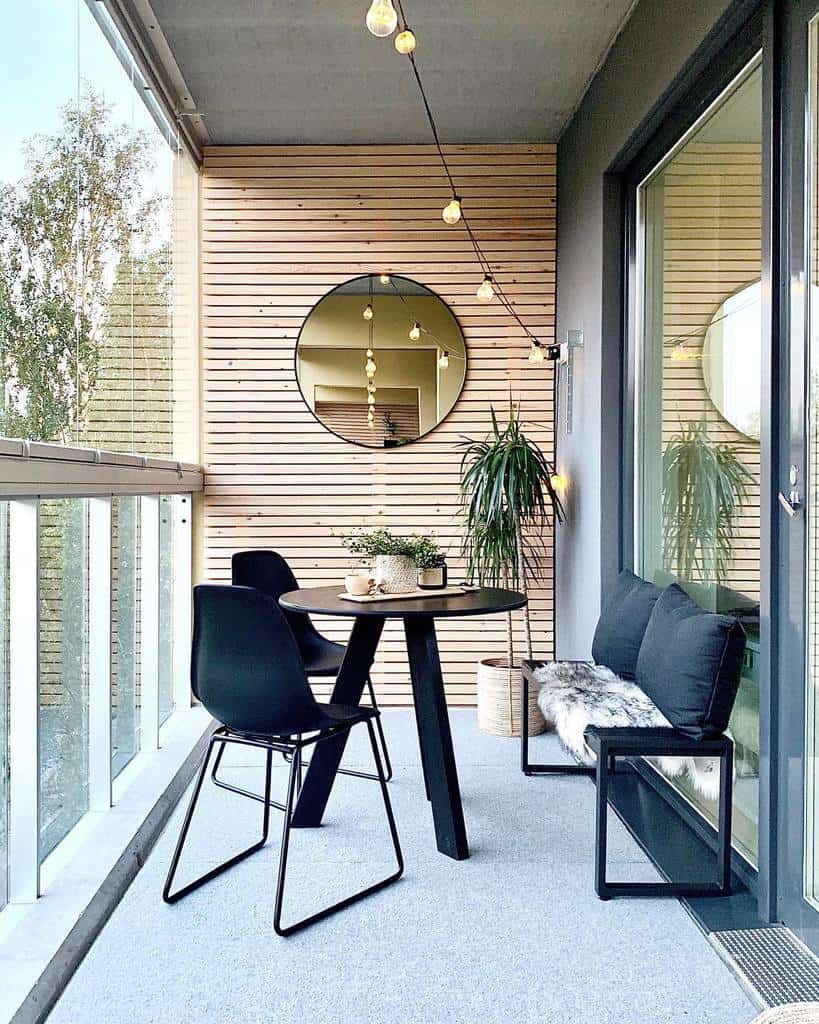 Modern balcony with black table and chairs, wooden wall paneling, string lights, and potted plants.
