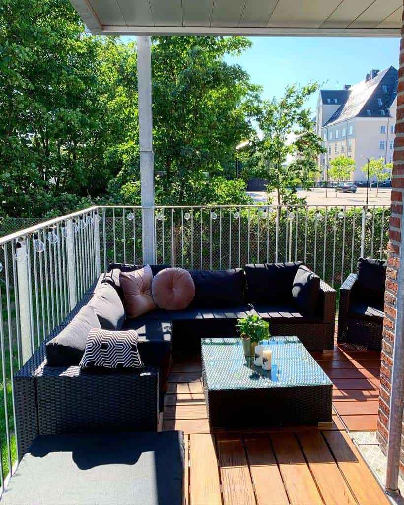Spacious balcony with a large black outdoor sectional, coffee table, and string lights.