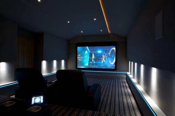 A cozy home theater with two seats, a large screen playing sci-fi, and ambient blue LED lighting