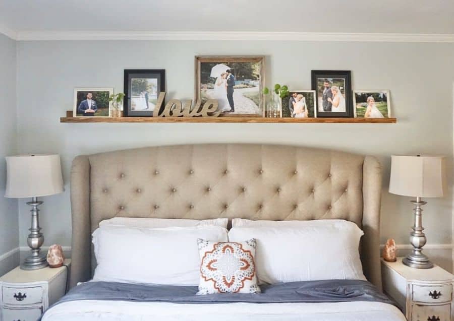 Cozy bedroom with tufted headboard, photo shelf above bed, and elegant bedside lamps.