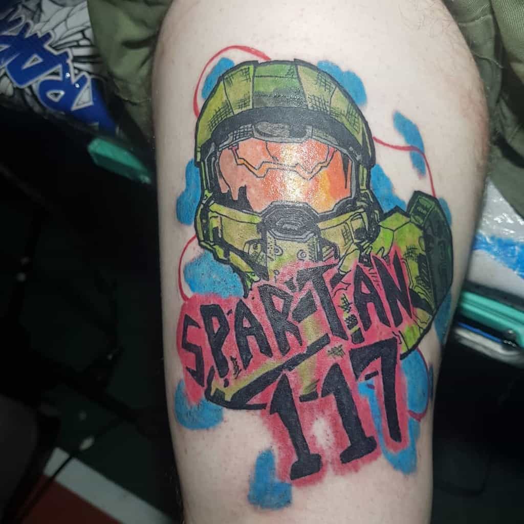 Bold Halo tattoo of Master Chief’s helmet with 'SPARTAN 117' in graffiti-style lettering, surrounded by vibrant blue and red splashes.