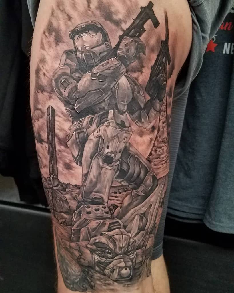 Epic black and gray Halo tattoo of Master Chief standing victorious over a fallen Elite, with a detailed battlefield background on the upper arm.