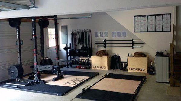 Garage gym with squat rack, lifting platforms, Rogue plyo boxes, and neatly organized equipment.