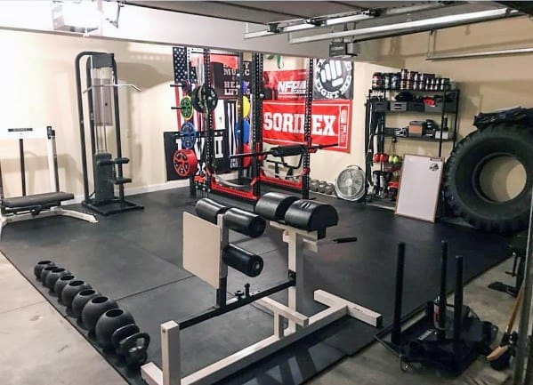 Garage gym with weight racks, kettlebells, sled, tire, and bodybuilding equipment.