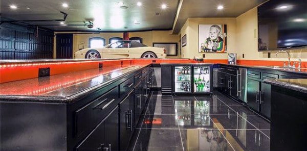 Luxurious home bar with sleek black countertops, a display fridge, and a vintage car parked in the garage