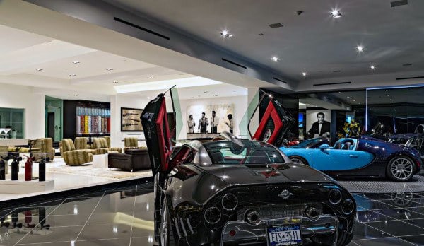 Luxury cars in a showroom with open doors, art pieces, and seating area visible in the garage-like setting