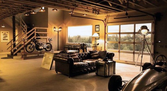 A stylish garage boasts leather furniture, a vintage motorcycle, and a race car beside large windows with a scenic view
