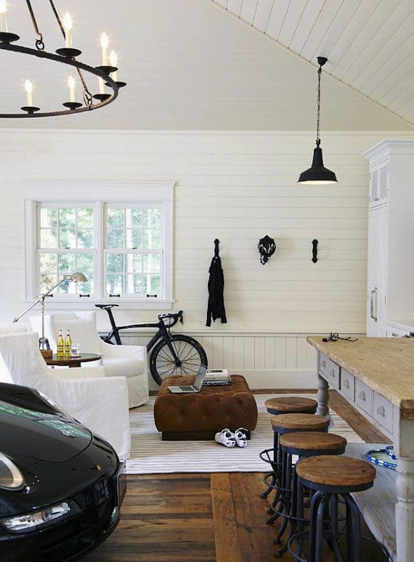 Cozy garage room with a bike, car front, bar stools, and a chandelier above a sofa and ottoman; white walls and wood floor