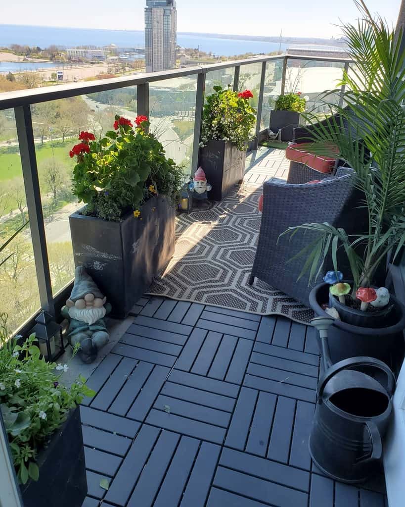 High-rise balcony with potted plants, gnome decor, outdoor seating, and a view of the city and water.