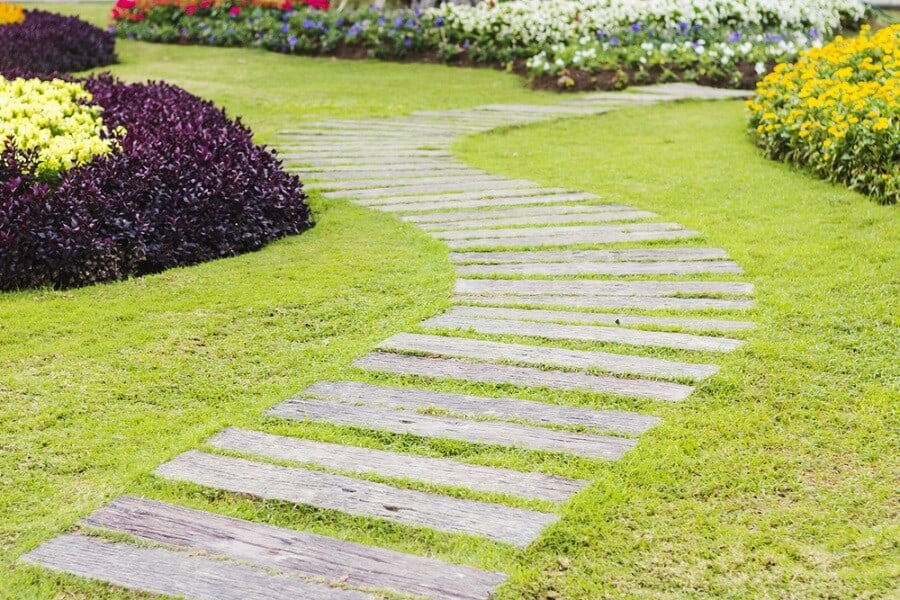Curved wooden walkway through a garden with green grass and colorful flowers