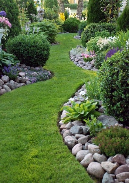 A lush garden path bordered with smooth stones, lined with vibrant plants and shrubs, creating a serene pathway