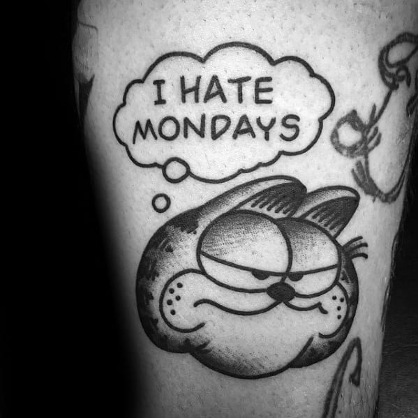 Bold black and gray Garfield tattoo with a grumpy face and 'I Hate Mondays' thought bubble—a classic, relatable design for humor lovers.