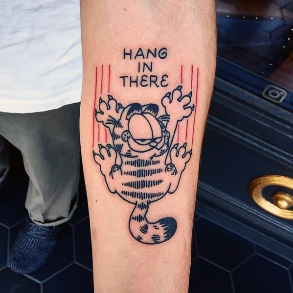 Garfield tattoo hanging by his claws with 'Hang in There' text—bold black ink with red scratch marks for a fun and motivational design.