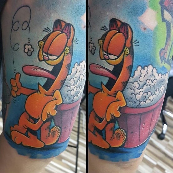 Vibrant Garfield tattoo with an exaggerated stretched-out look, relaxing near a tub of popcorn—funny and bold cartoon-style design.