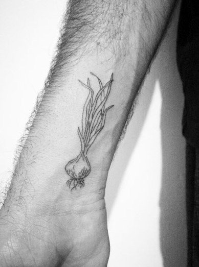 Minimalist garlic tattoo on the wrist with fine linework, featuring long stems and roots for a simple yet elegant botanical design.