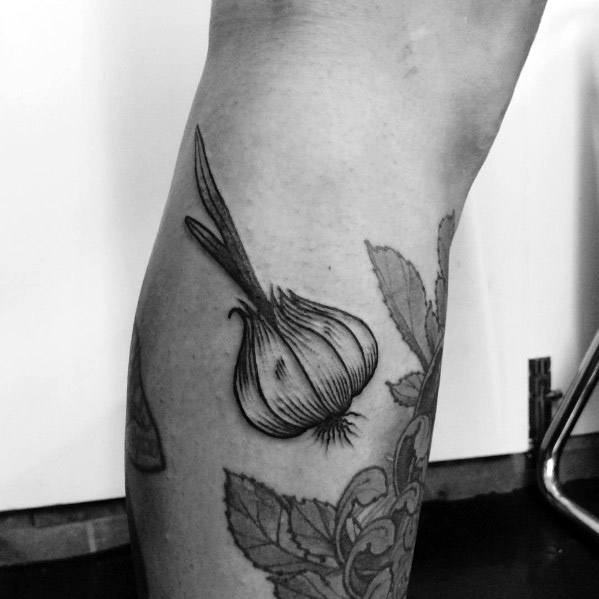 Black and grey garlic tattoo on the leg with fine linework and shading, featuring long stems for a bold and natural botanical design.