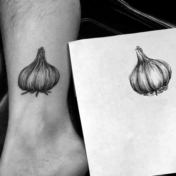 Realistic black and grey garlic tattoo on the ankle, closely matching the original sketch with fine shading and detailed texture.