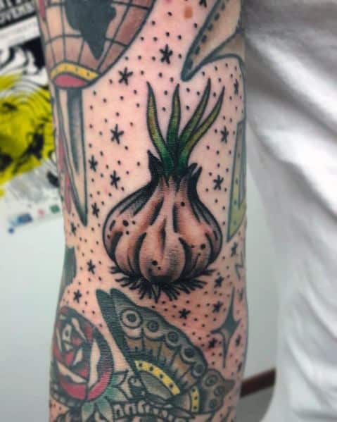 Traditional-style garlic tattoo with bold outlines, vibrant shading, and decorative star details, blending seamlessly with surrounding tattoos.