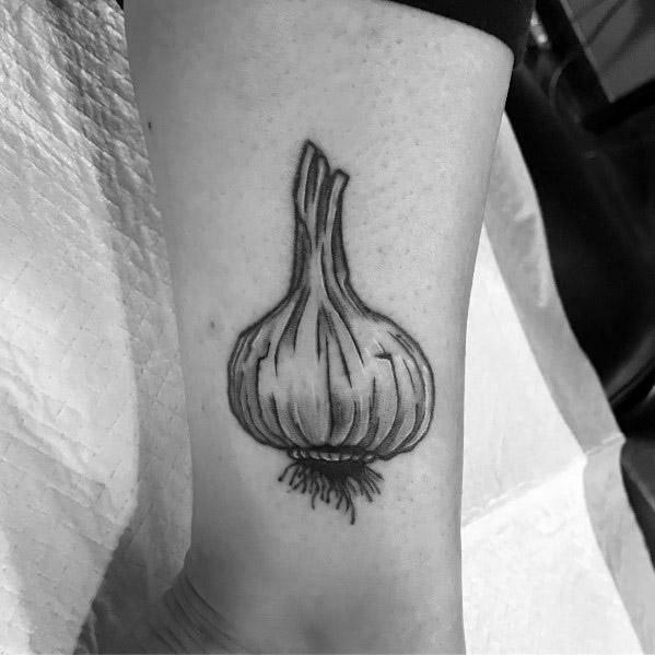 Realistic black and grey garlic tattoo on the ankle with fine shading and detailed texture, creating a bold and organic botanical design.