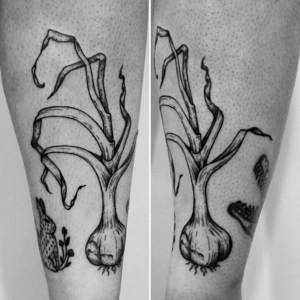 Black and grey garlic tattoo with long, twisting leaves and fine line shading, creating a bold and organic botanical design on the leg.