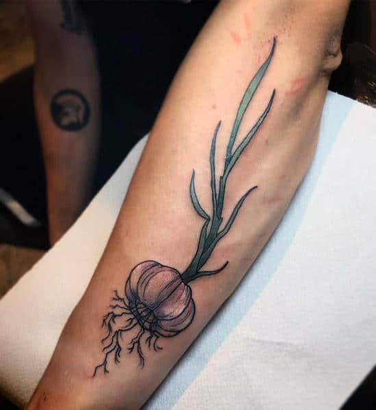 Delicate garlic tattoo with fine linework, soft shading, and flowing green stems, creating an elegant and natural botanical design on the forearm.