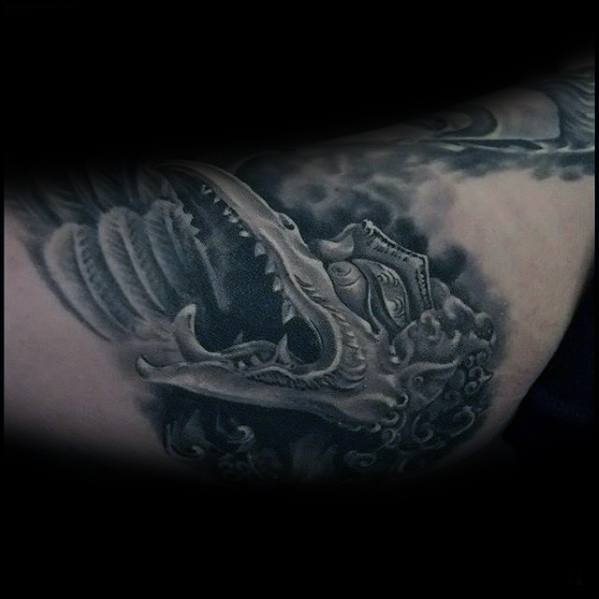 Dark Garuda tattoo featuring a fierce open-mouthed face with detailed shading and cloudy background, creating a dramatic and intense look.