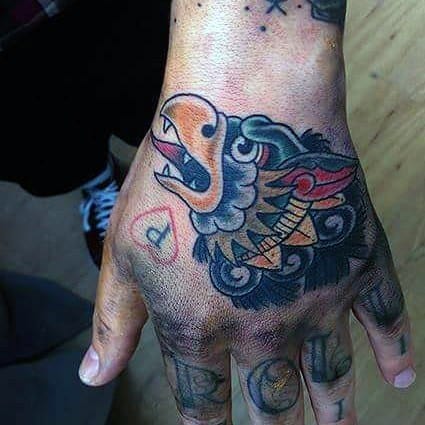 Small Garuda tattoo on the hand with bold traditional-style colors, featuring a stylized beaked face, clouds, and sharp detailing.