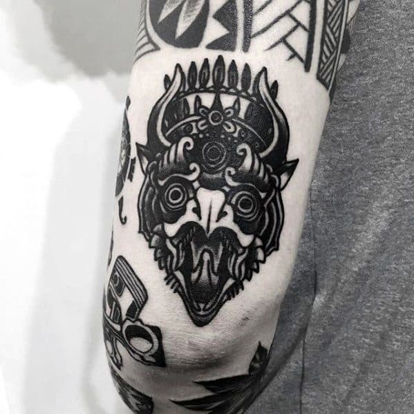 Garuda tattoo design with bold black lines and tribal influence, featuring a horned head placed on the back of the arm.