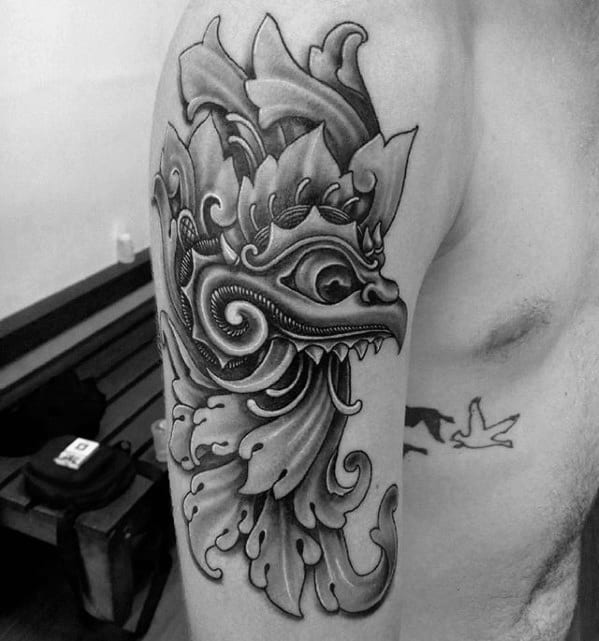 Garuda tattoo design with a sharp-beaked face and flowing ornamental shapes, placed on the upper arm in bold black and grey ink.