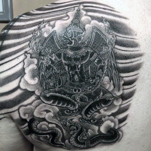 Garuda tattoo design on the shoulder with intricate detailing, showing the deity grasping serpents amid swirling clouds and shaded lines.