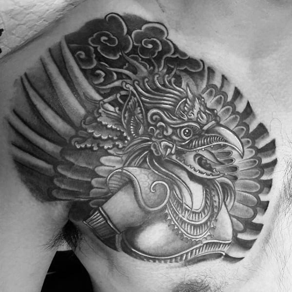 Garuda tattoo design on the chest showing a fierce winged figure in profile with bold feathers, jewelry, and swirling cloud motifs.