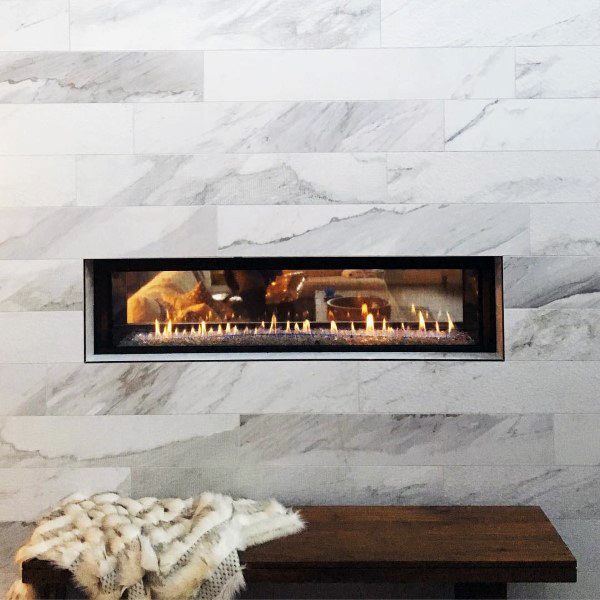 Linear gas fireplace with a black frame set in a white marble tile surround.