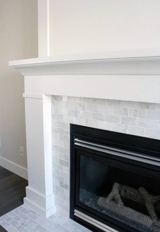 White fireplace with a classic wood mantel, marble subway tile surround, and a gas firebox.