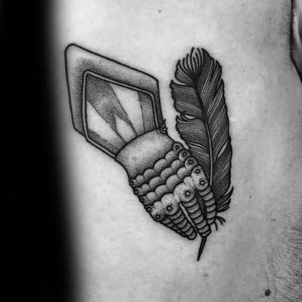 Black and grey tattoo of a medieval gauntlet gripping a feather and a diamond-shaped crystal, detailed with dotwork shading.