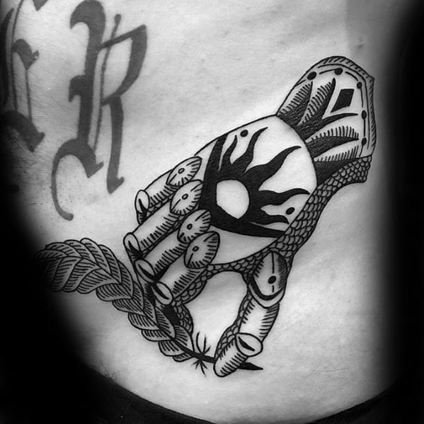 Black ink tattoo of a detailed armored hand holding a feather, with a bold sun emblem on the gauntlet and ornamental patterns.