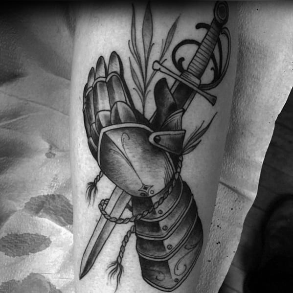 Black and grey tattoo of a crossed armored gauntlet and sword, detailed with rope and feather accents for a classic medieval look.