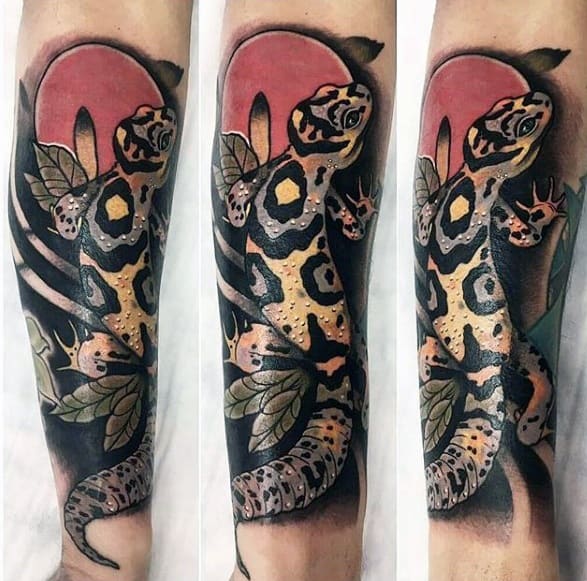 Leopard gecko forearm tattoo with bold spots, leafy background, and a red sun-like circle adding contrast and depth.
