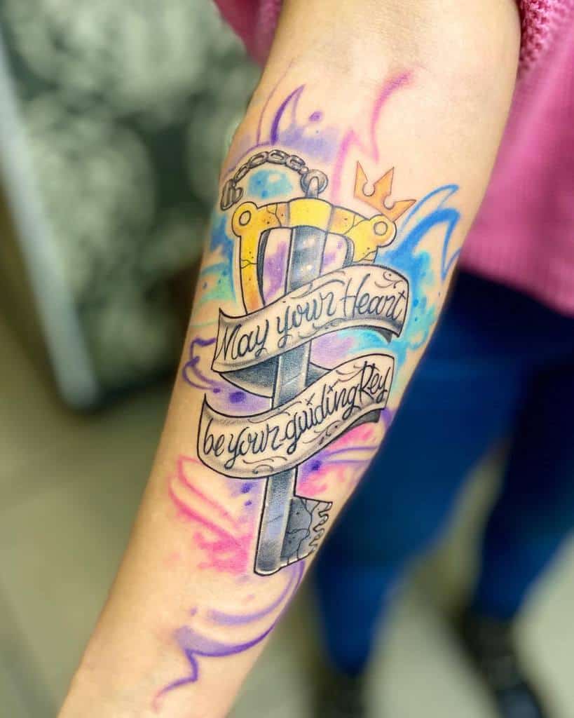 Colorful Kingdom Hearts tattoo featuring a Keyblade with a banner reading 'May your heart be your guiding key,' surrounded by vibrant swirls.