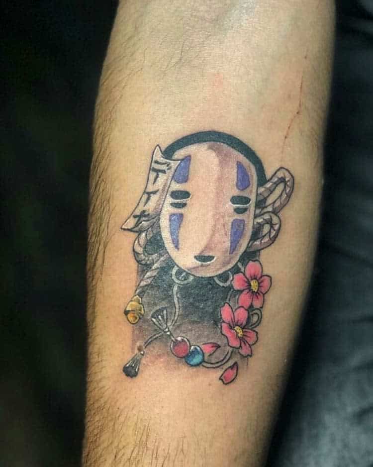 Elegant Spirited Away tattoo of No-Face adorned with braided ropes, charms, and cherry blossoms, blending soft shading with vibrant colors
