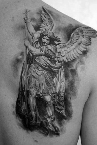 A detailed black and grey tattoo on the upper back depicting a powerful angel holding a sword, with large wings and a dramatic, cloud-like backdrop.