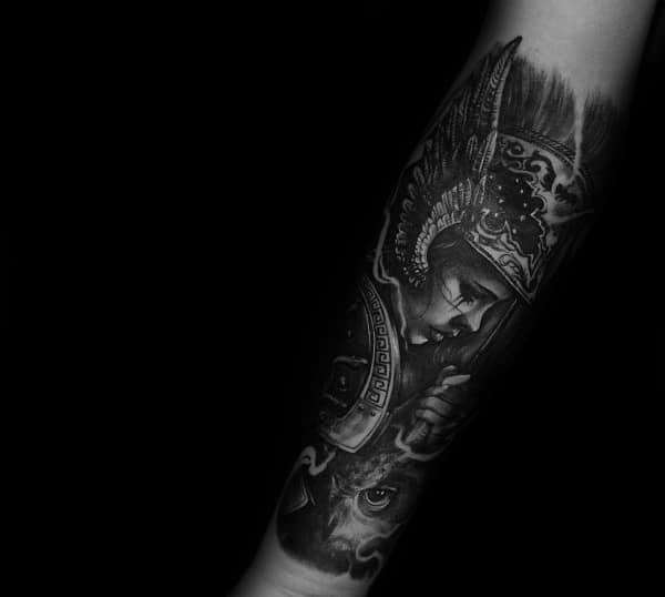 Dark and detailed Athena tattoo on forearm with winged helmet, downward gaze, and fierce owl beneath in black and grey realism