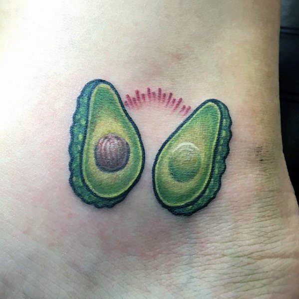 Cute avocado halves tattoo on the ankle, one with a pit and one without, joined by a pink heartbeat-style line for a playful touch.
