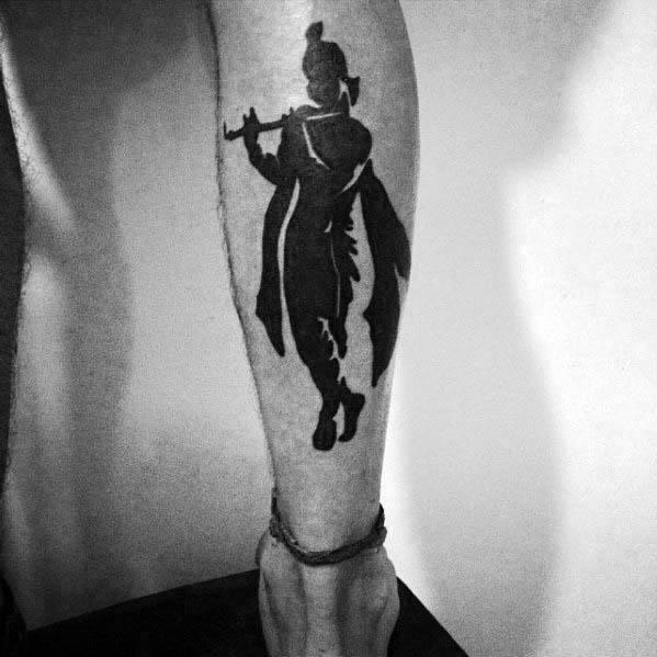 Bold black silhouette tattoo of Lord Krishna playing the flute, capturing his iconic pose with flowing garments and topknot hairstyle.