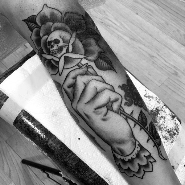 Tattoo of a hand holding a needle threading through a skull-faced flower