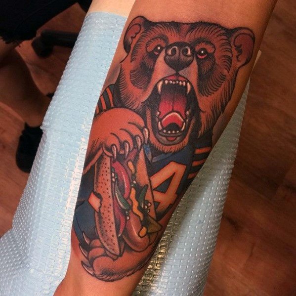 Tattoo of a roaring bear holding a hot dog, showcasing bold outlines and vibrant colors on the forearm.