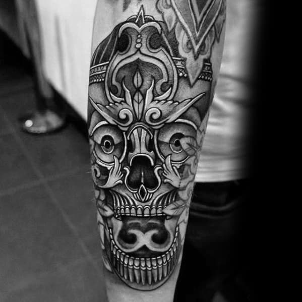 Black and grey Tibetan skull tattoo on the forearm with bold lines, symmetrical patterns, and stylized ornamental detailing.